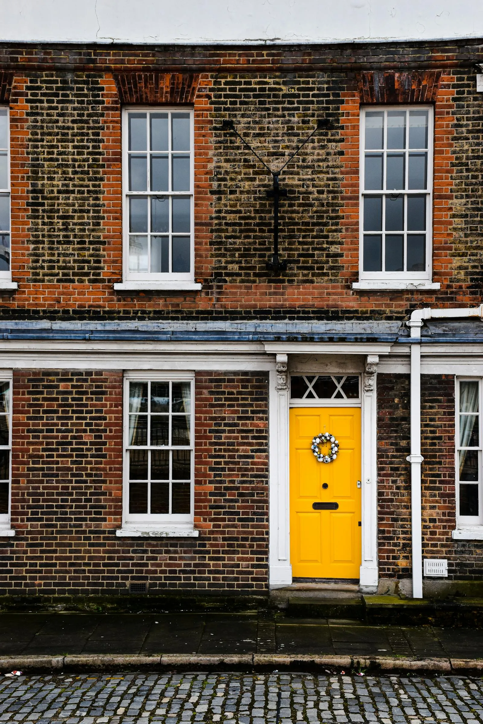 A handsome red-brick UK terrace with sash windows and a striking yellow front door — period terraced stock representative of the late-Victorian housing that defines Romsey.